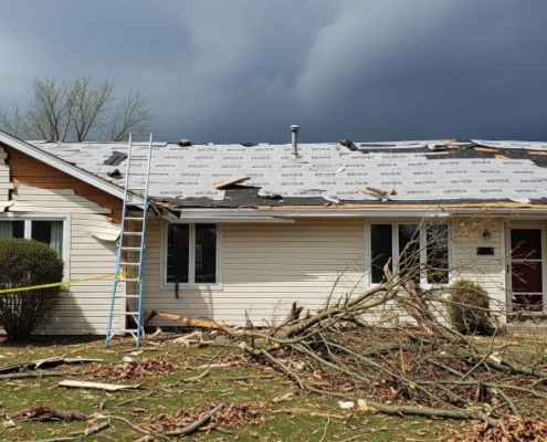 Storm-damaged Minnesota home with missing shingles, broken siding, and debris in the yard as repairs begin